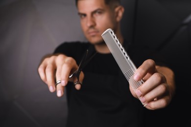 Photo of Hairdresser near dark wall, focus on professional comb