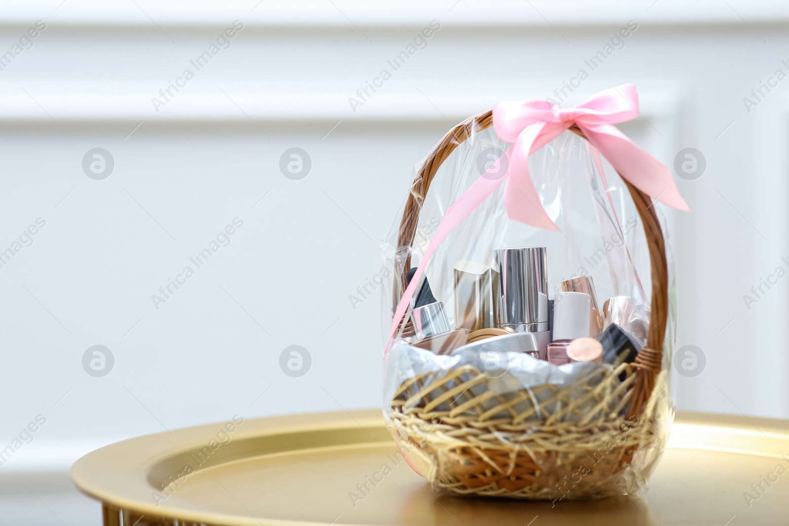 Photo of Gift set in wicker basket on golden table near white wall. Space for text