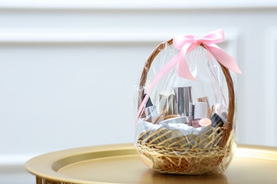 Photo of Gift set in wicker basket on golden table near white wall. Space for text