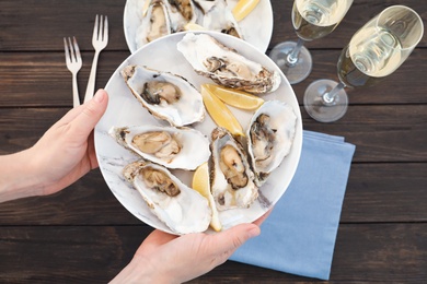 Photo of Top view of woman with plate of fresh oysters over table, focus on hands