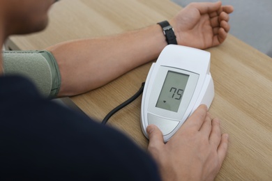 Man checking blood pressure with sphygmomanometer at table indoors, closeup. Cardiology concept