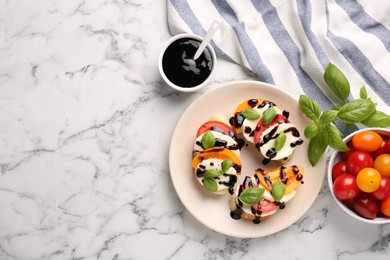 Photo of Delicious bruschettas with mozzarella cheese, tomatoes, balsamic vinegar and ingredients on white marble table, flat lay. Space for text