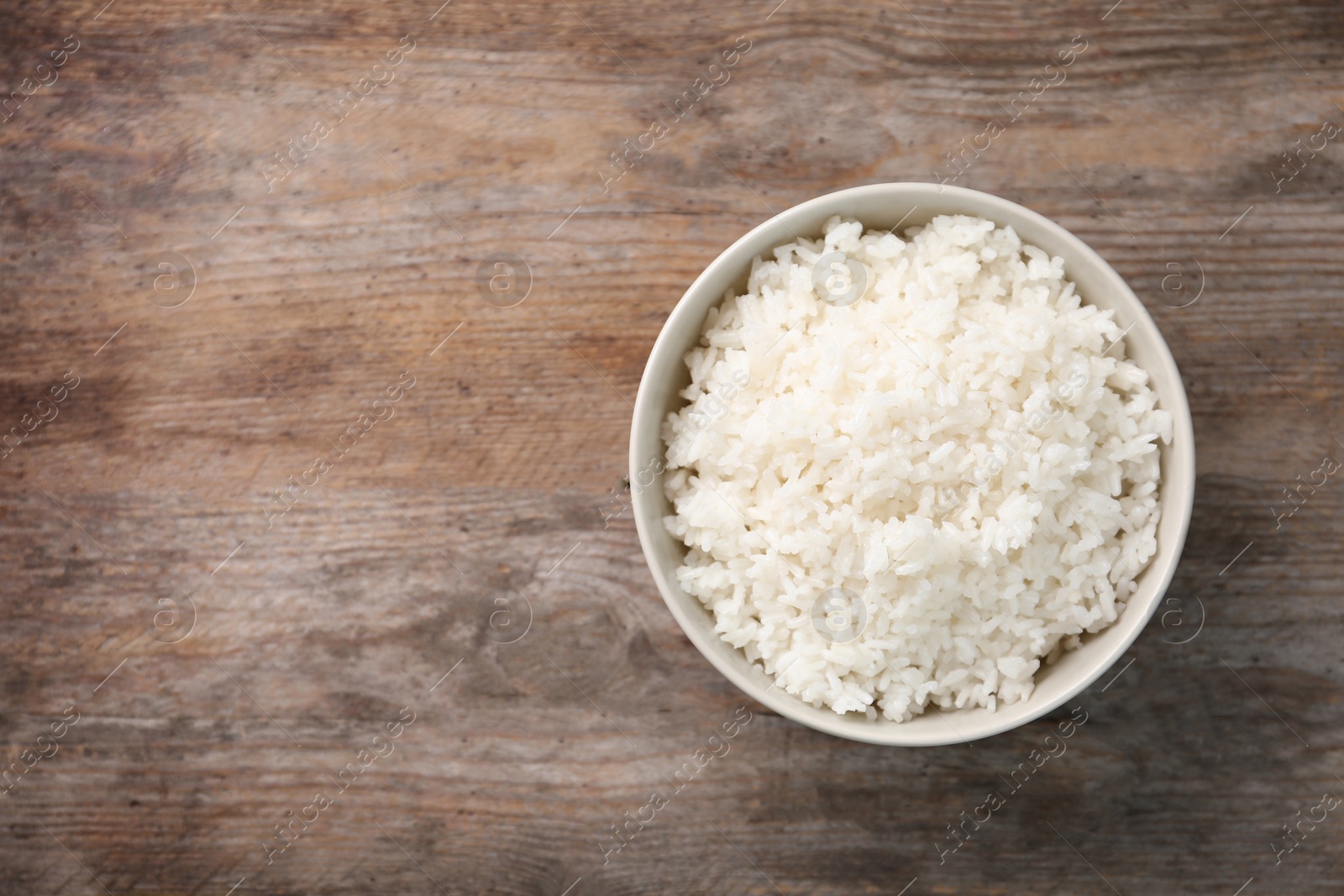 Photo of Bowl of boiled rice on wooden background, top view with space for text