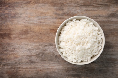 Bowl of boiled rice on wooden background, top view with space for text