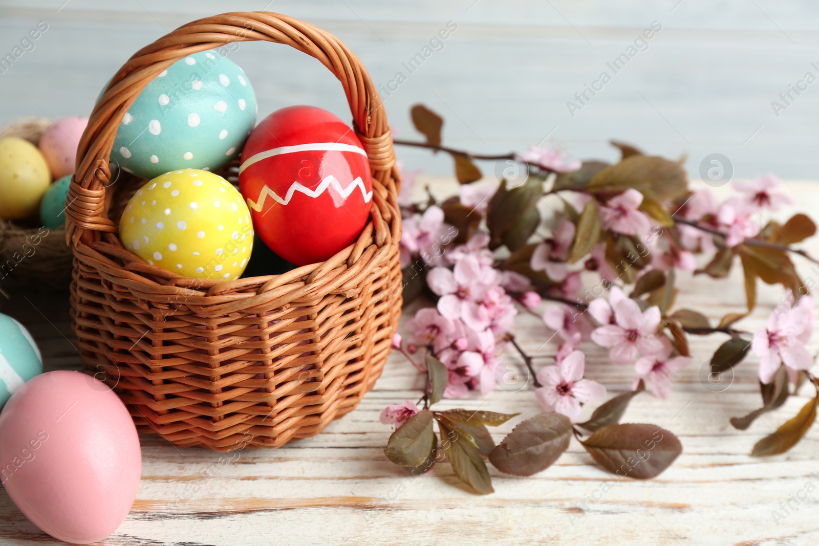 Photo of Painted Easter eggs in wicker basket and blossoming branches on wooden table