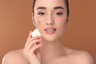 Photo of Woman applying foundation on face with makeup sponge against brown background