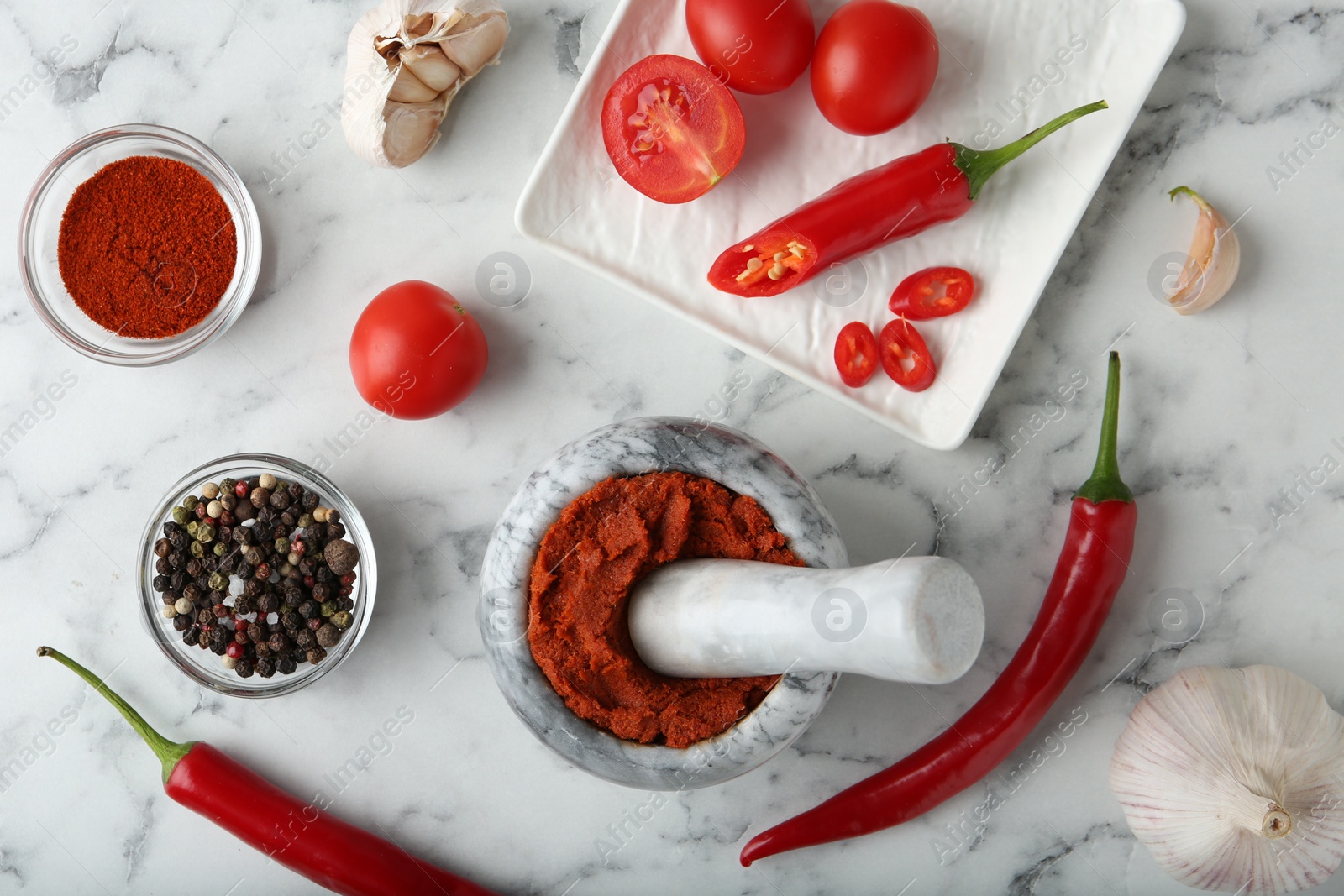 Photo of Red curry paste in mortar and ingredients on white marble table, flat lay