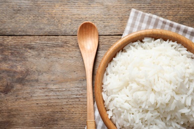 Bowl of delicious rice on wooden table, top view with space for text