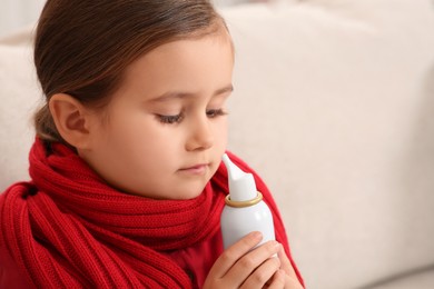 Photo of Cute little girl holding nasal spray on sofa, closeup
