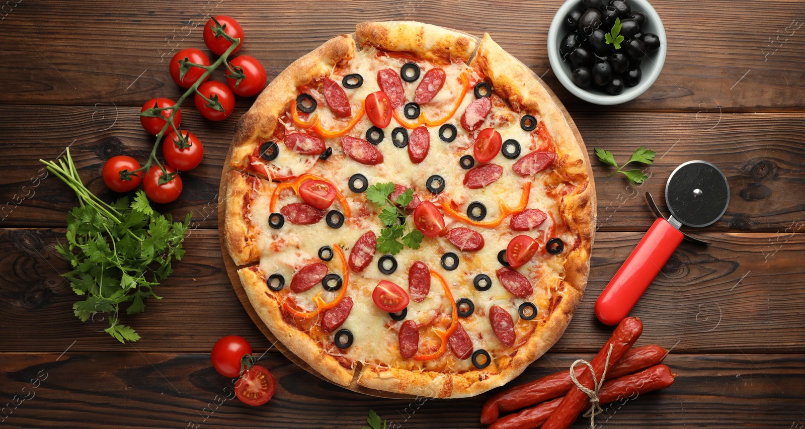 Photo of Tasty pizza, ingredients and cutter on wooden table, top view