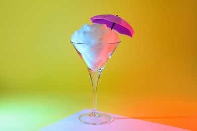 Photo of Beautiful martini glass with cotton candy and umbrella on color background
