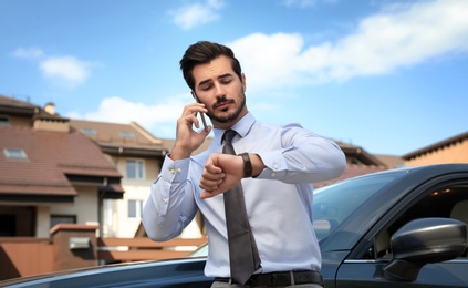 Photo of Attractive young man talking on phone near luxury car outdoors