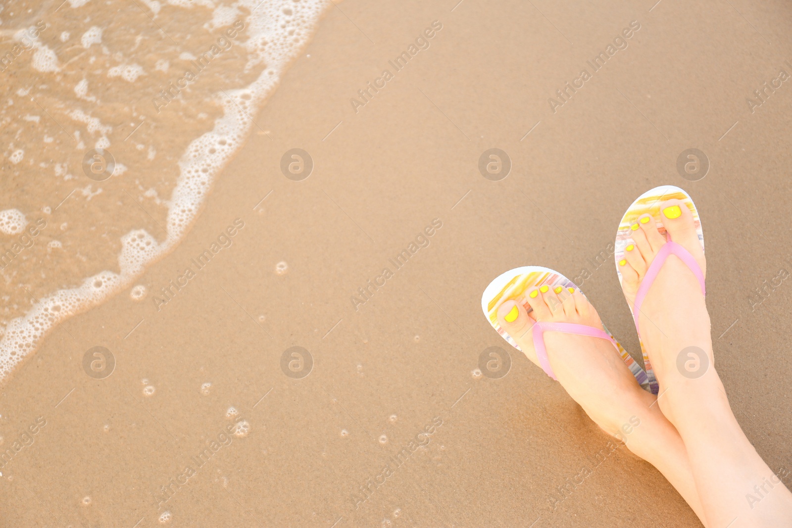 Photo of Closeup of woman with stylish flip flops on sand near sea, space for text. Beach accessories