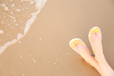 Photo of Closeup of woman with stylish flip flops on sand near sea, space for text. Beach accessories