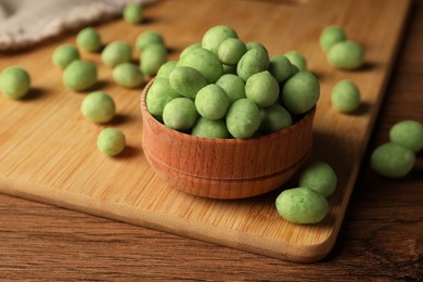 Tasty wasabi coated peanuts on brown wooden table, closeup