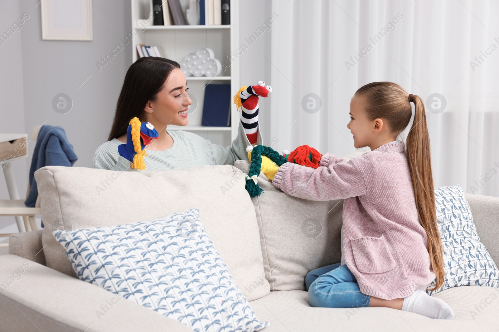 Photo of Happy mother and daughter playing with sock puppets together at home