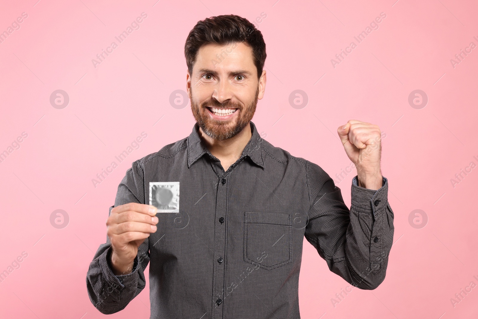 Photo of Emotional man holding condom on pink background. Safe sex