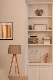 Photo of Stylish shelves with different decor elements and lamp in room. Interior design