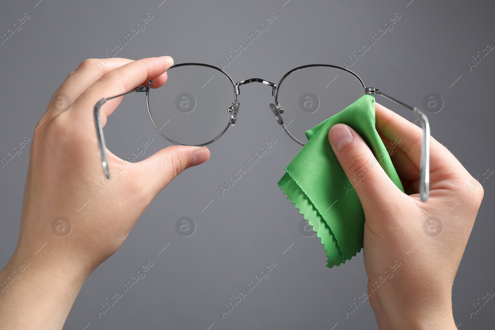 Photo of Woman wiping glasses with microfiber cloth on light grey background, closeup