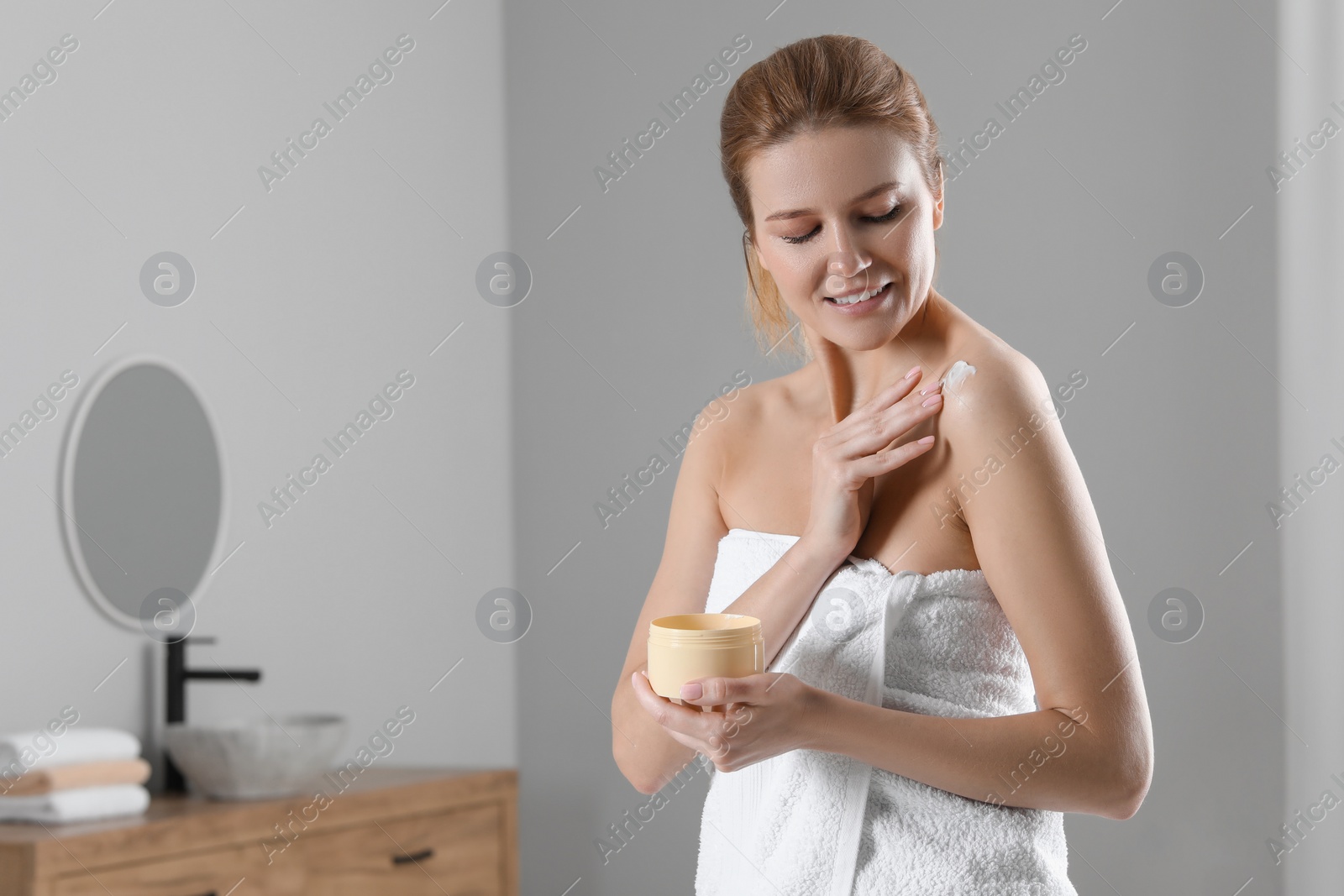 Photo of Happy woman applying body cream onto shoulder in bathroom, space for text