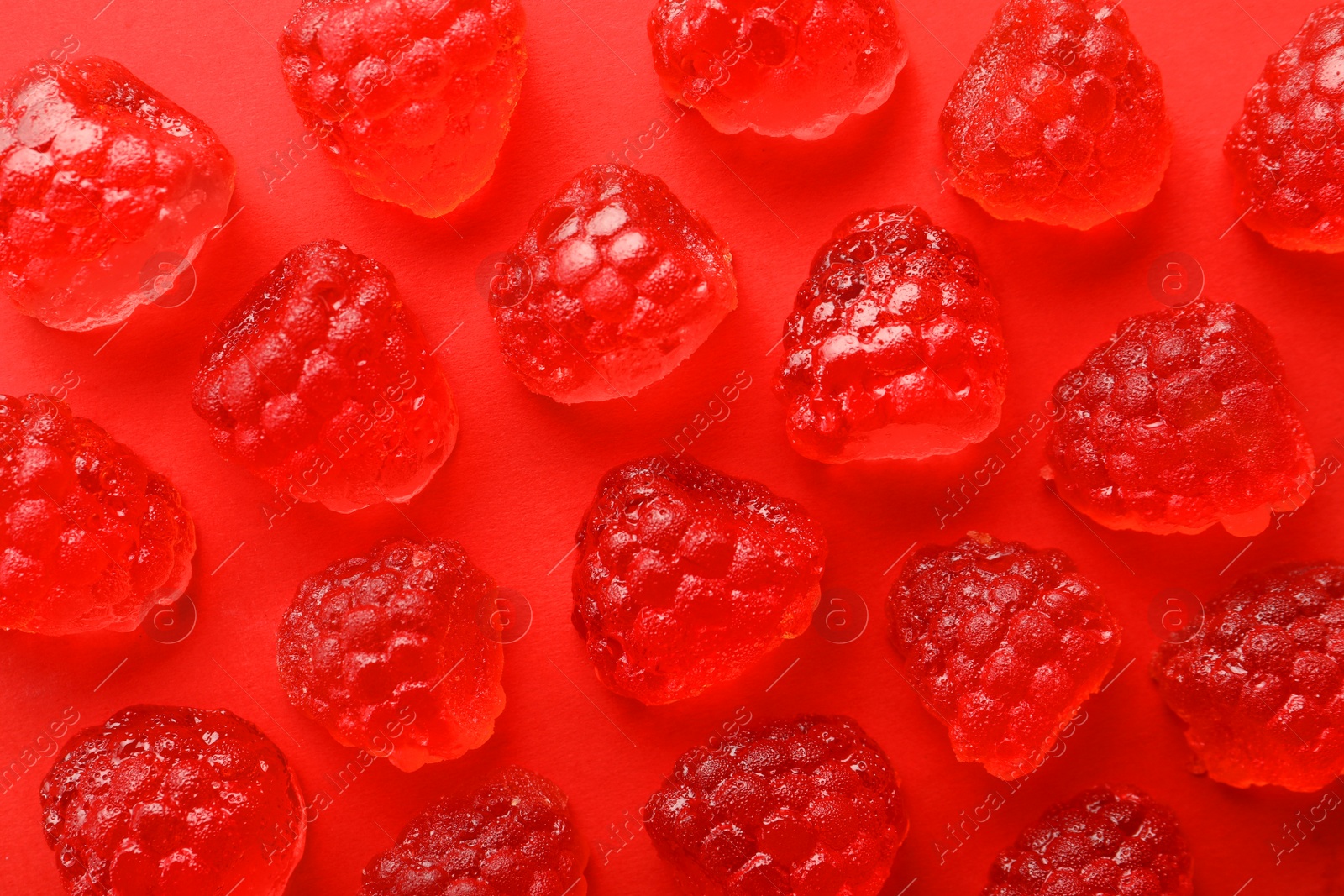 Photo of Delicious gummy raspberry candies on red background, flat lay