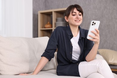 Beautiful young housewife using smartphone on sofa at home