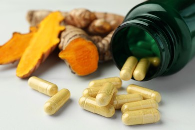 Photo of Turmeric roots, pills and bottle on white table, closeup