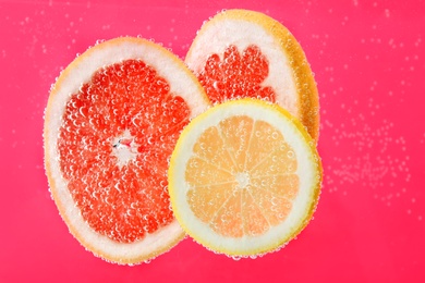 Photo of Slices of different citrus fruits in sparkling water on pink background