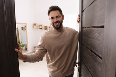 Photo of Happy man standing near door. Invitation to come indoors
