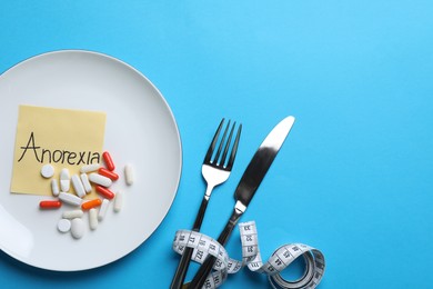 Flat lay composition with word Anorexia, table setting and pills on light blue background. Space for text