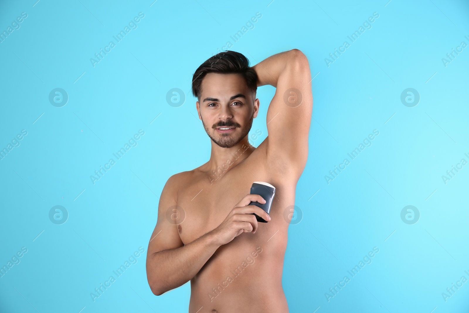 Photo of Young man using deodorant on color background