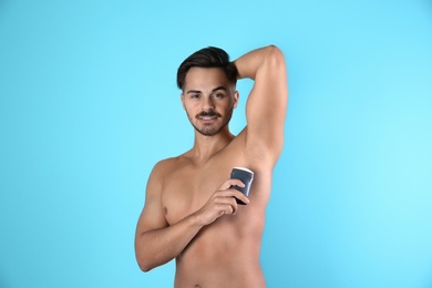 Young man using deodorant on color background