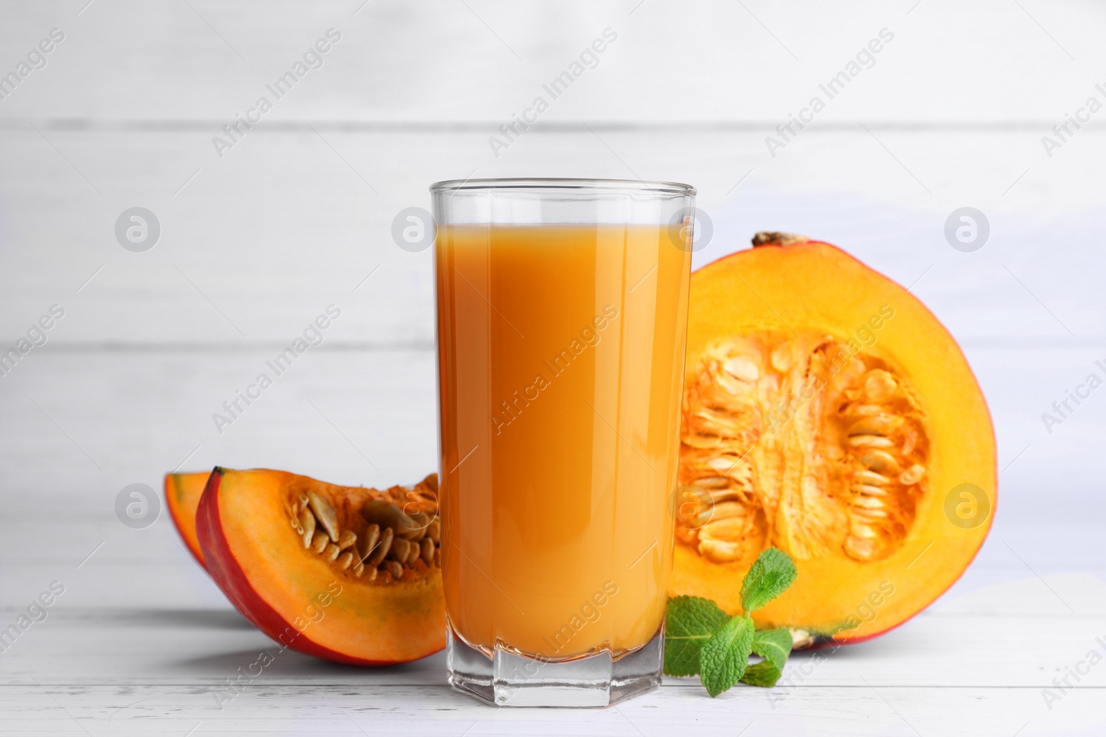 Photo of Tasty pumpkin juice in glass and cut pumpkin on white wooden table
