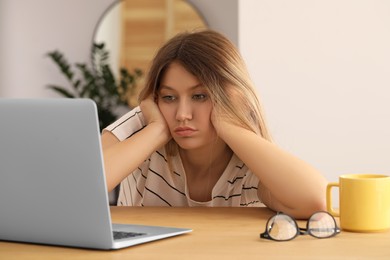 Photo of Sleepy young woman with laptop at wooden table indoors