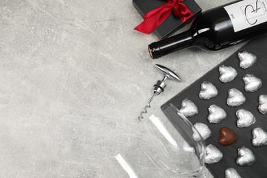 Photo of Bottle of red wine, glasses, heart shaped chocolate candies, corkscrew and gift box on light grey textured table, flat lay. Space for text