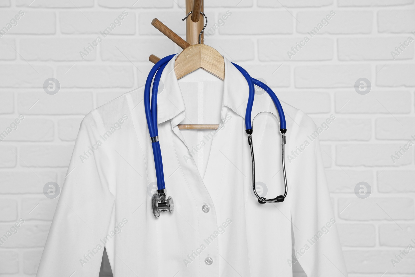 Photo of Medical uniform and stethoscope hanging on rack near white brick wall