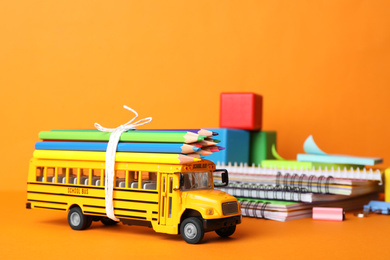 Photo of School bus model and stationery on orange background. Transport for students