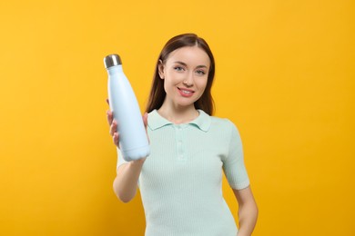 Photo of Beautiful young woman with thermos bottle on orange background