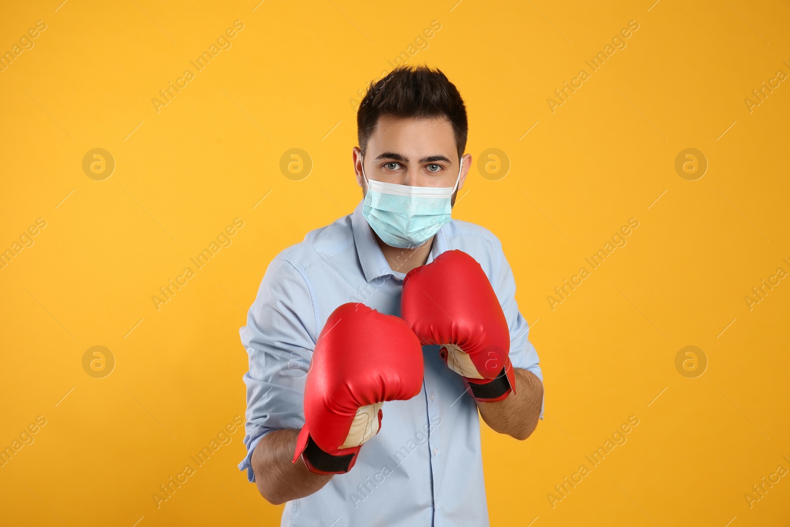 Photo of Man with protective mask and boxing gloves on yellow background. Strong immunity concept