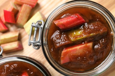 Jars of tasty rhubarb jam and cut stems on wooden table, closeup