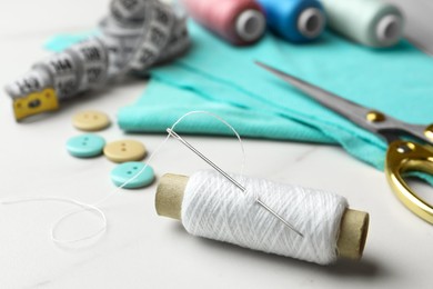 Threads and other sewing supplies on white marble table, closeup