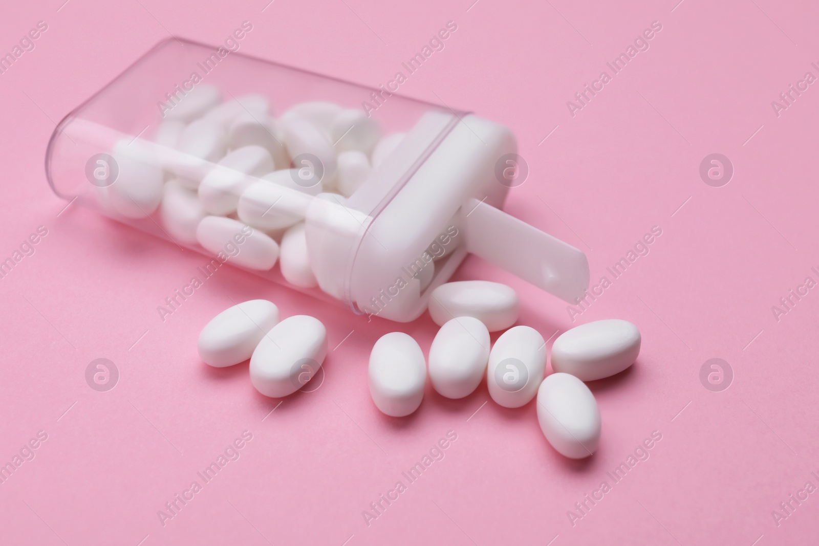 Photo of Tasty dragee candies and container on pink background, closeup