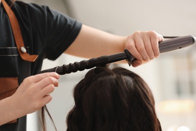 Hair styling. Hairdresser curling woman's hair in salon, closeup