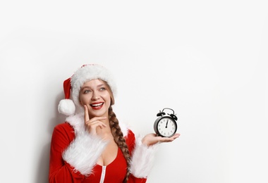 Photo of Beautiful Santa girl with alarm clock on light background. Christmas eve