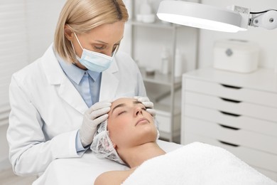 Dermatologist examining patient`s face under lamp in clinic