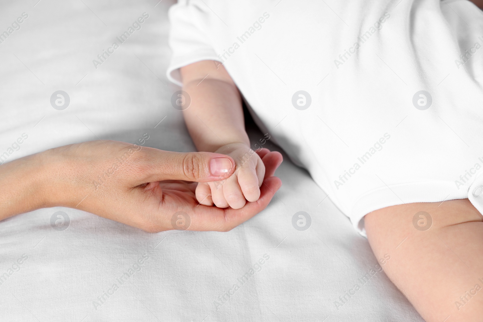 Photo of Mother holding hand of her little baby on bed, closeup