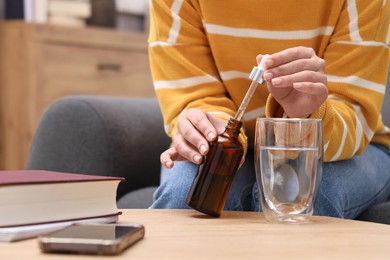 Photo of Woman dripping food supplement into glass of water on wooden table indoors, closeup