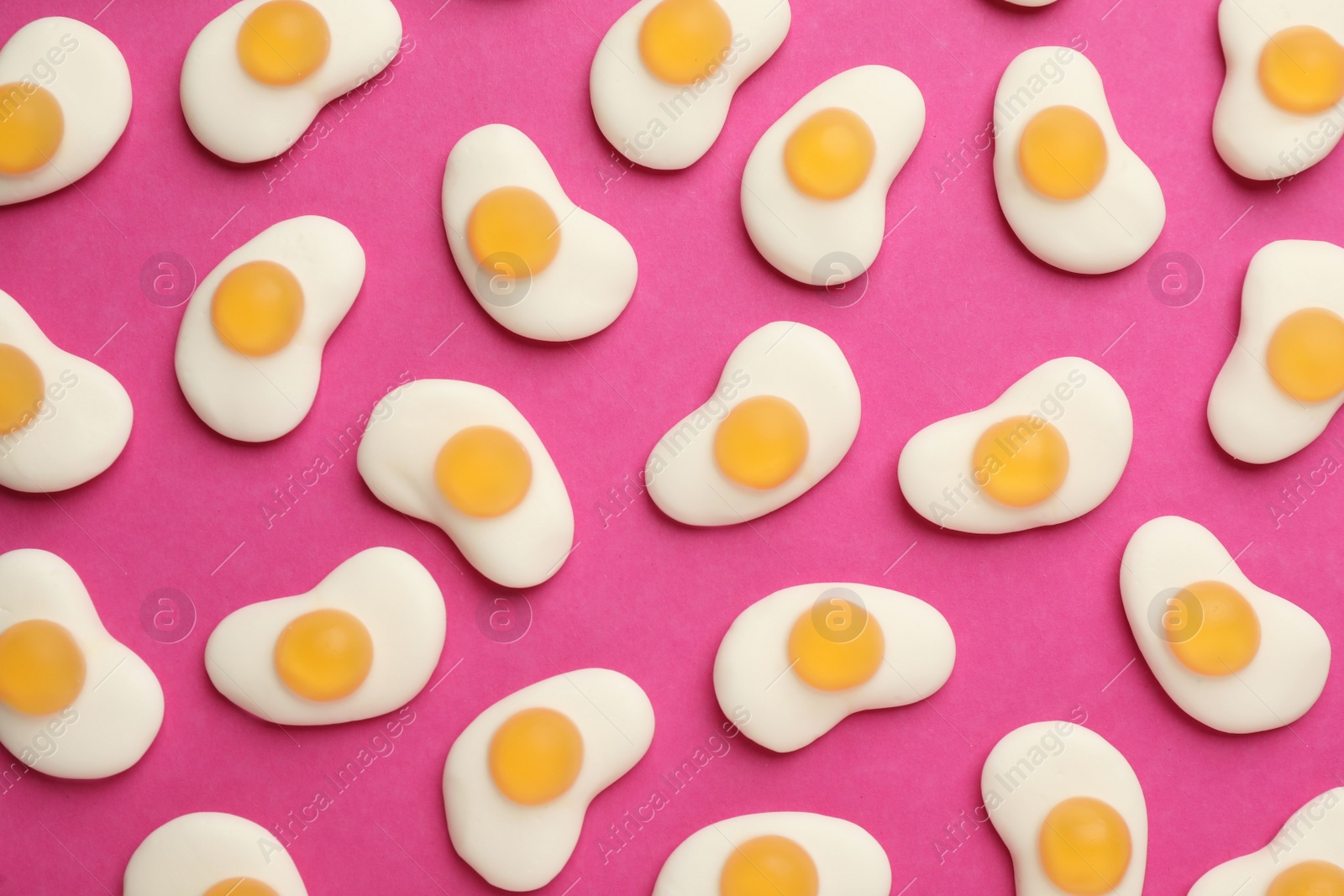 Photo of Tasty jelly candies in shape of egg on pink background, flat lay