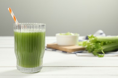 Photo of Glass of celery juice and fresh vegetables on white wooden table, space for text