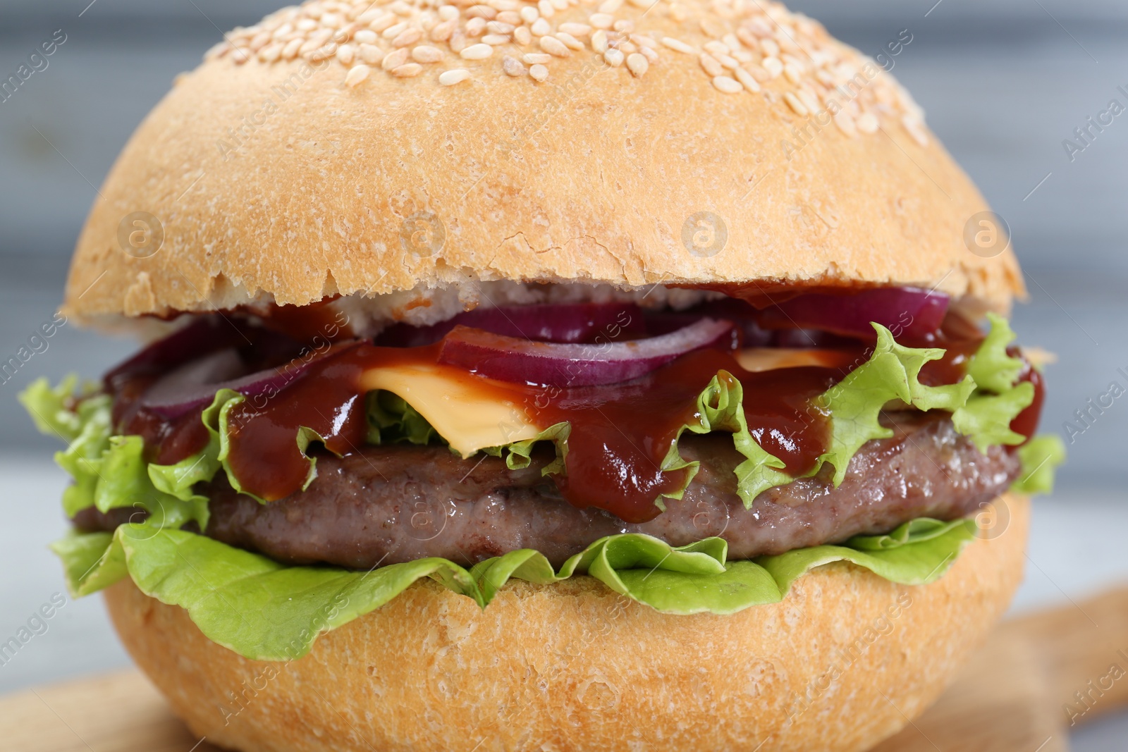 Photo of Delicious cheeseburger with lettuce, onion, ketchup and patty on blurred background, closeup